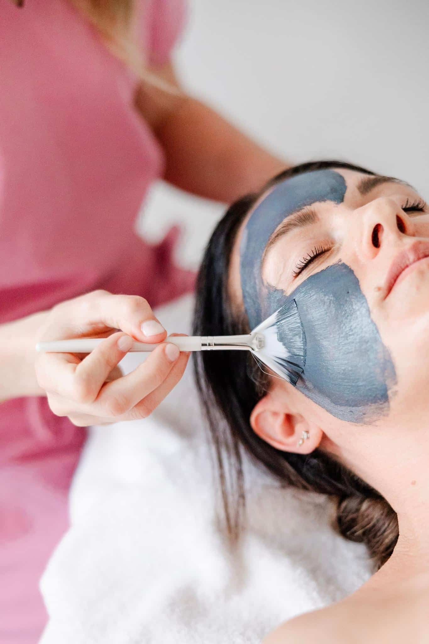 Callie applying a detoxifying mask to a woman lying down with her eyes closed