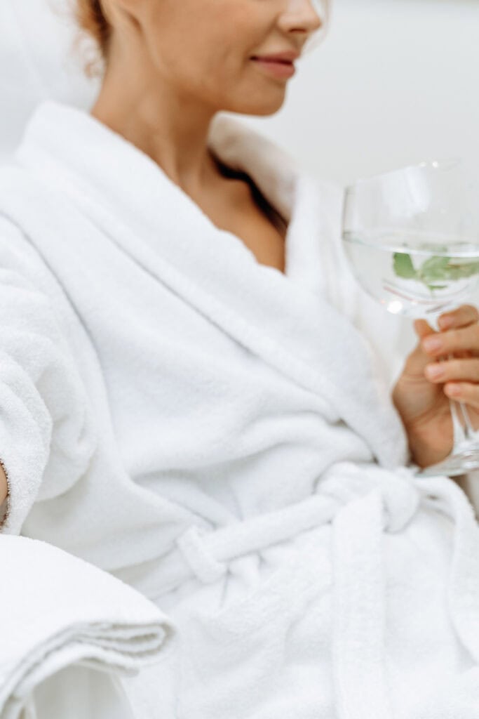 Close up of calm female patient sitting with tube and needle during IV infusion. Girl holding glass with lemon water and relaxing