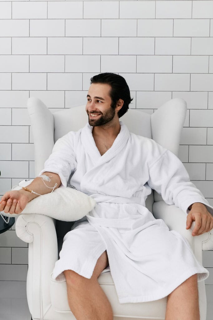 a happy man wearing a white bath rube receiving an IV therapy